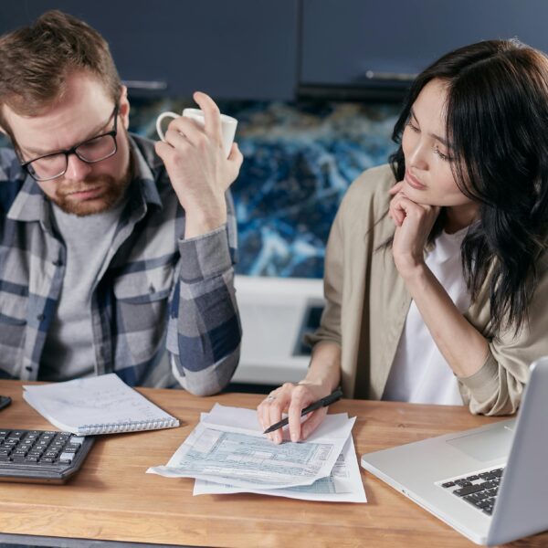 A couple reviews bills and documents on a laptop while discussing household finances.